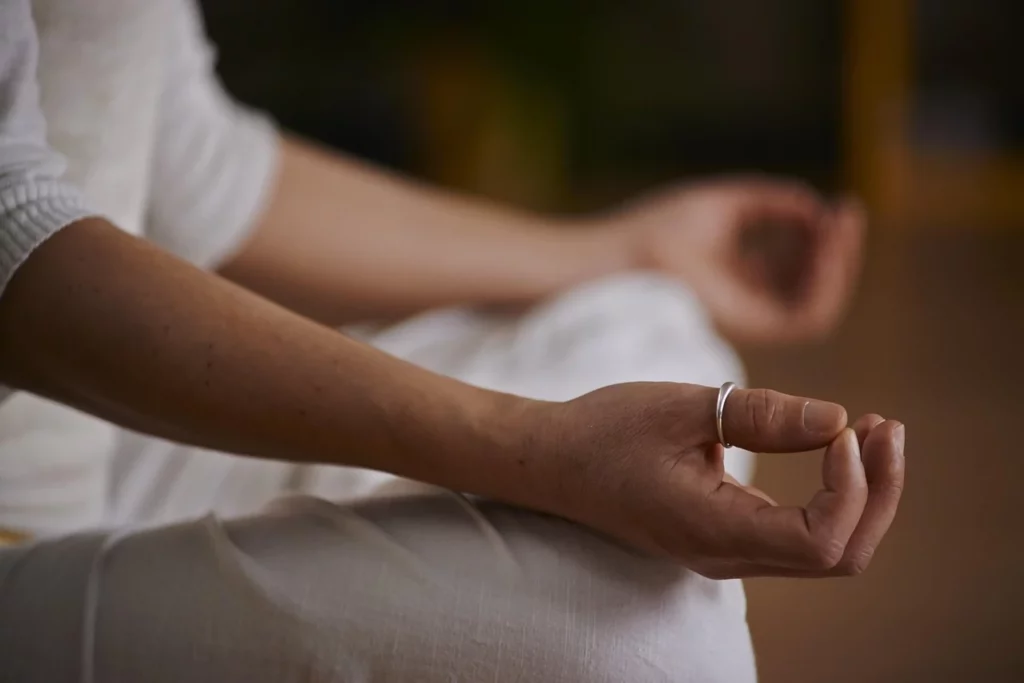 Persoon zit rustig in meditatiehouding met de handen ontspannen op de knieën.