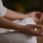 Persoon zit rustig in meditatiehouding met de handen ontspannen op de knieën.