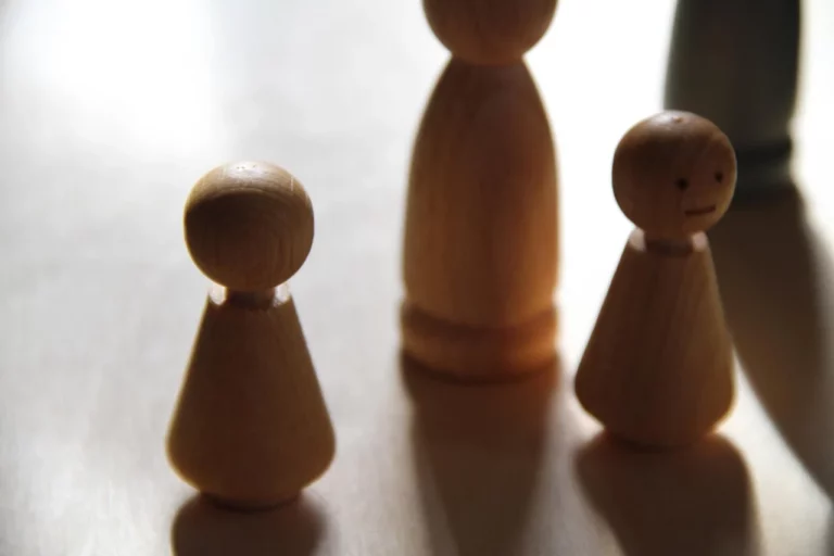 Houten poppetjes staan in een familieopstelling op een lichte tafel.