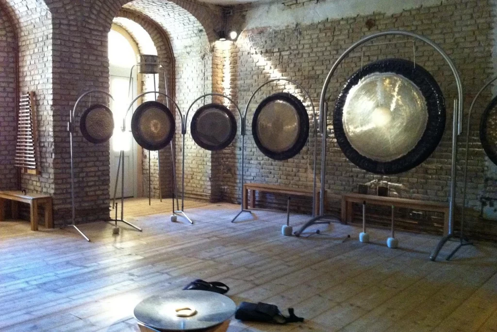 Een rij grote gongs staat opgesteld in een lichte ruimte met bakstenen muren.