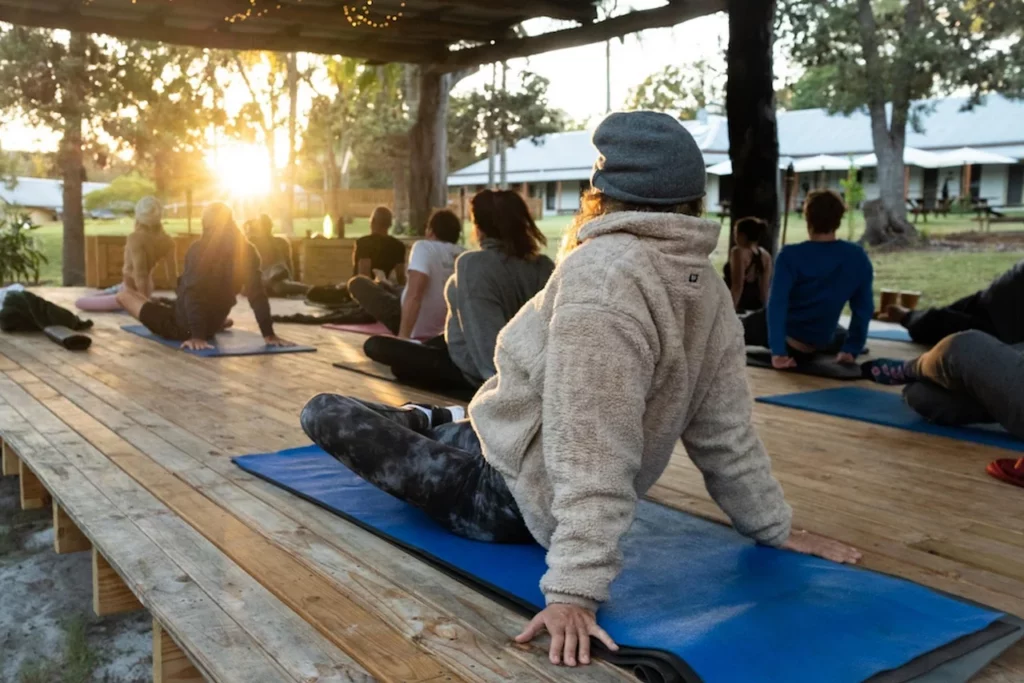 Deelnemers zitten op yogamatten tijdens een rustige buitenles onder een houten overkapping.